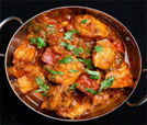 A pan filled with vibrant chicken curry and vegetables, set against a sleek black background, showcasing culinary excellence.