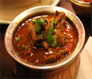 A bowl of hearty stew with meat and vegetables, showcasing the flavors of Indian and Nepali cuisine at a restaurant table.