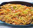 A fork rests beside a skillet of chicken and noodles, highlighting a flavorful Indian and Nepali culinary experience.