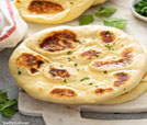 A cutting board adorned with warm, baked naan breads, representing the finest in Indian and Nepali culinary traditions.