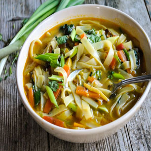 A wooden table displays a bowl of hearty vegetable and noodle soup, highlighting the best of Indian and Nepali culinary traditions.